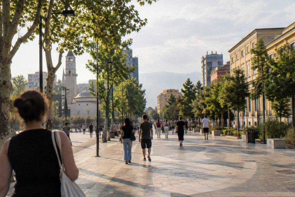 People walking along a tree-lined central street in Tirana on a warm afternoon
