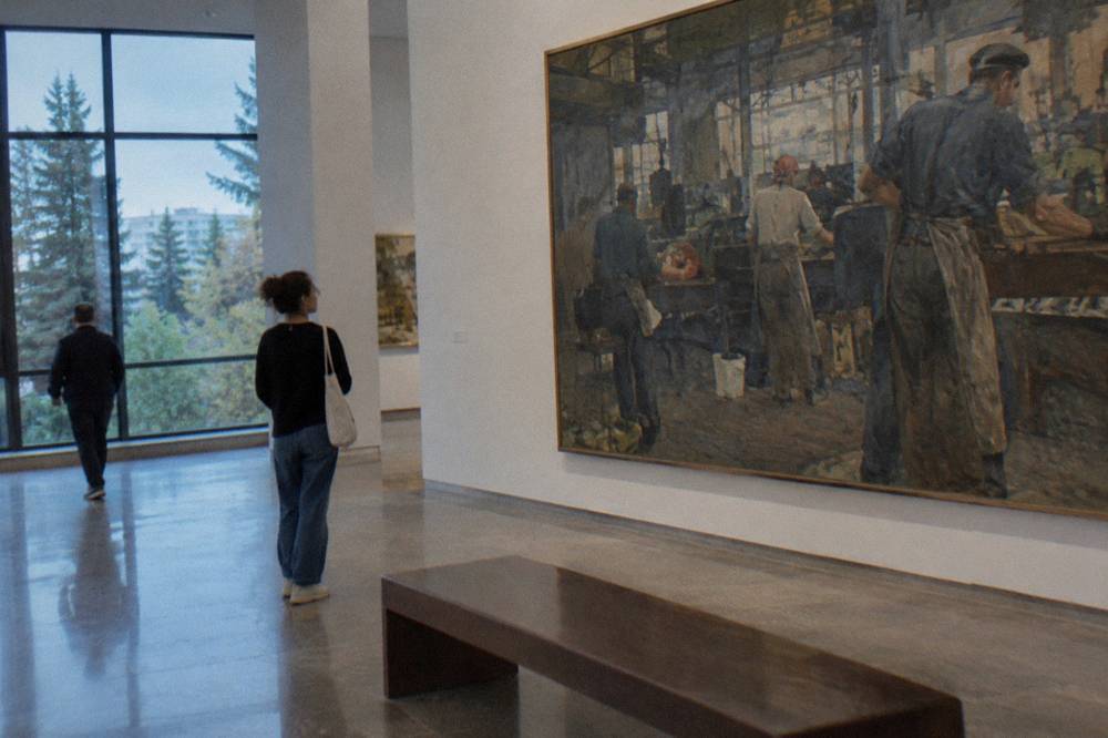 Large painting of workers in a factory hanging in a museum gallery