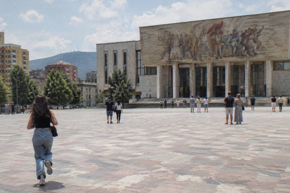 Visitors standing on the paved expanse of Skanderbeg Square looking toward the museum facade
