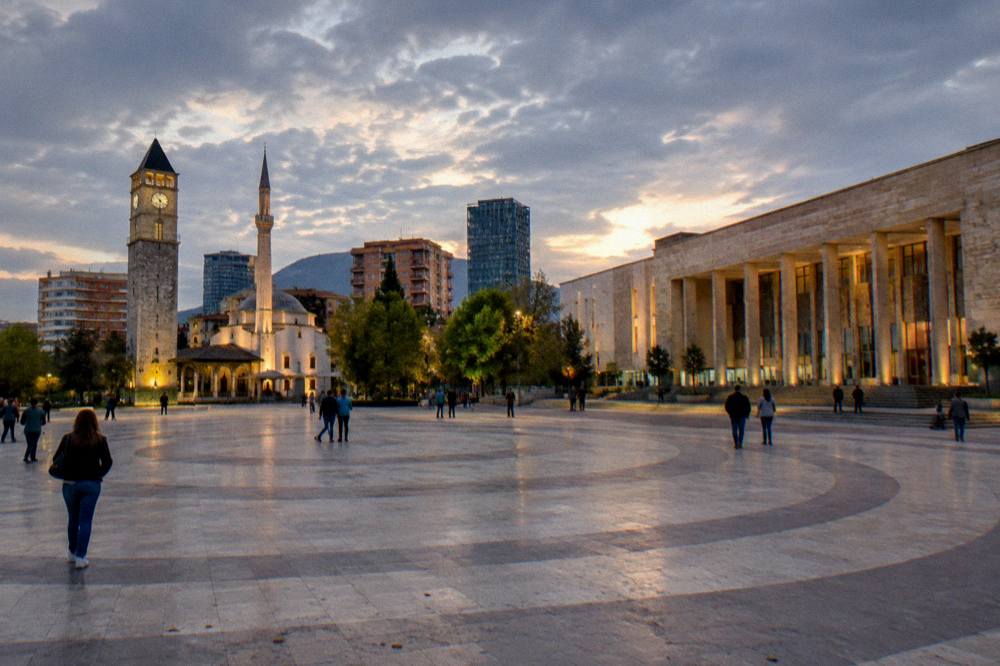 The museum facade and square at dusk with city lights coming on in Tirana