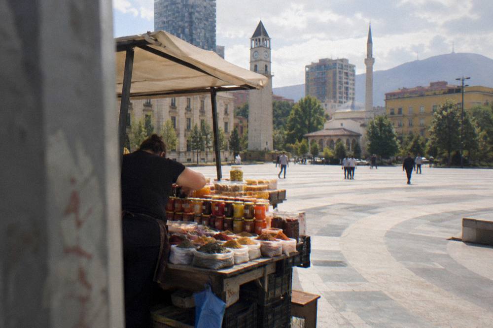 A vendor arranging jars of preserves and spices on a market stall in Tirana
