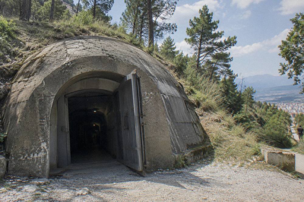 Close view of a mushroom-shaped concrete bunker set in grass at the Postblloku memorial in Tirana