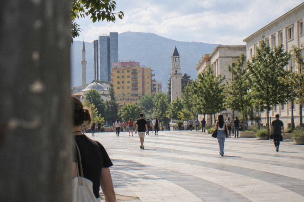 People walking along a wide boulevard in central Tirana with government buildings on one side