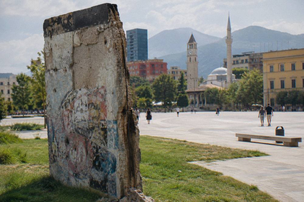 A fragment of the Berlin Wall displayed on grass at the Postblloku memorial in Tirana