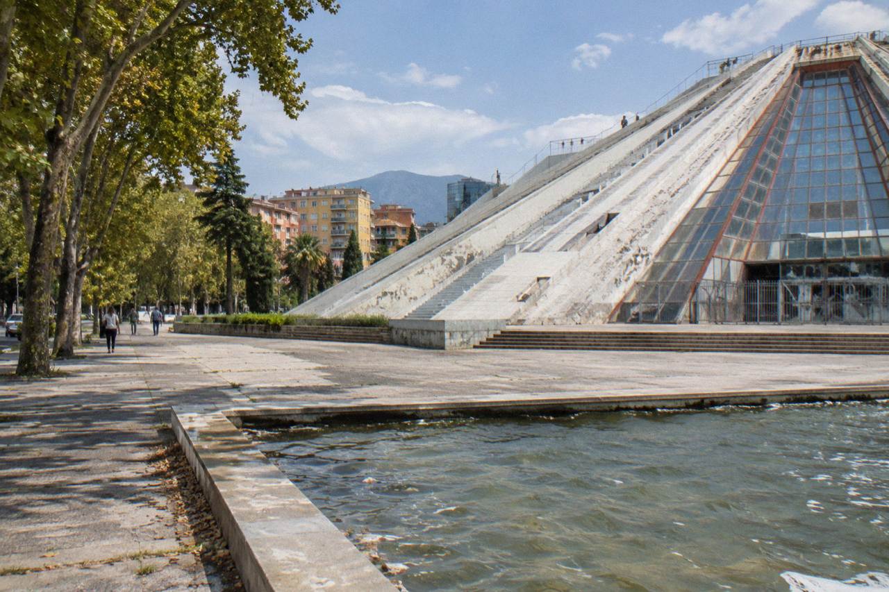 The sloped concrete and glass exterior of the Pyramid of Tirana under a daytime sky