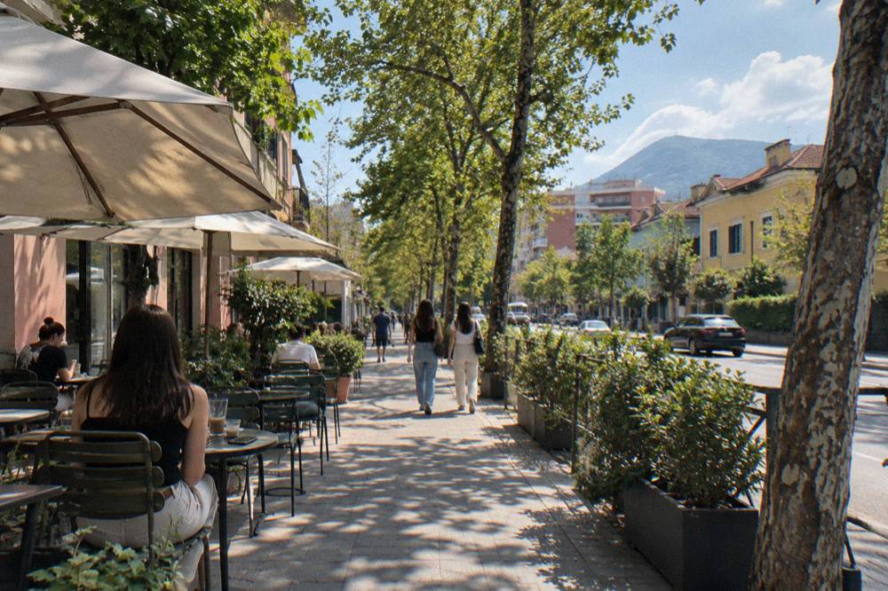 A tree-lined street in the Blloku quarter of Tirana with cafe tables along the pavement
