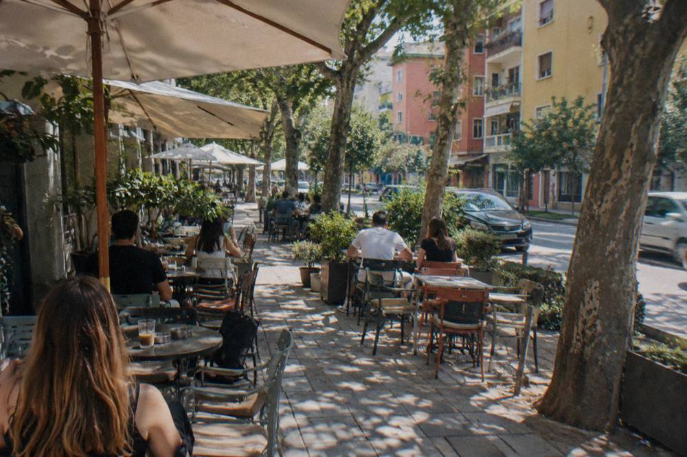People seated at outdoor cafe tables on a leafy street in Blloku in the late afternoon