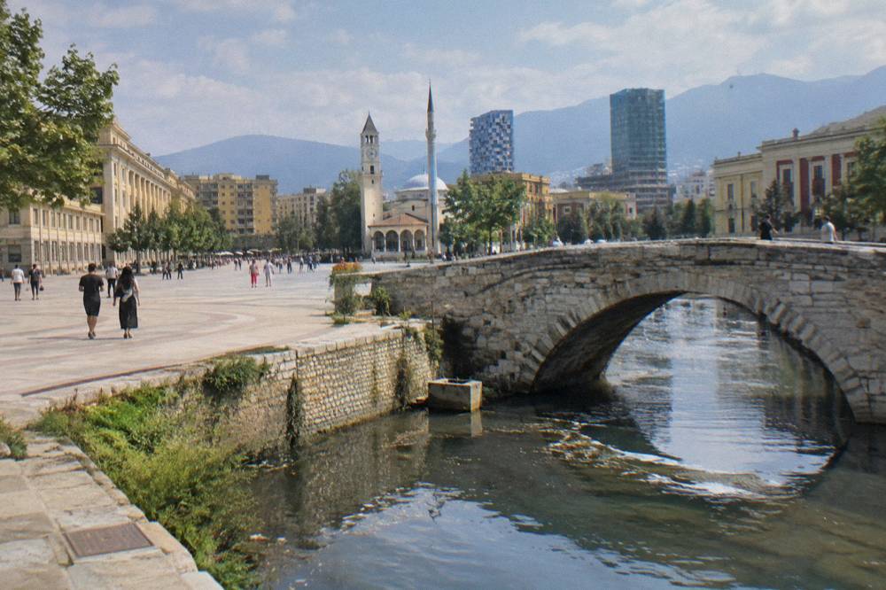 Old stone bridge arch reflected in a narrow channel of water in Tirana