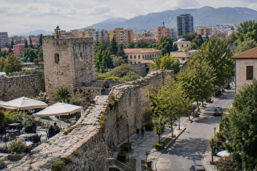 A quiet daytime street beside the castle walls with the city rising behind