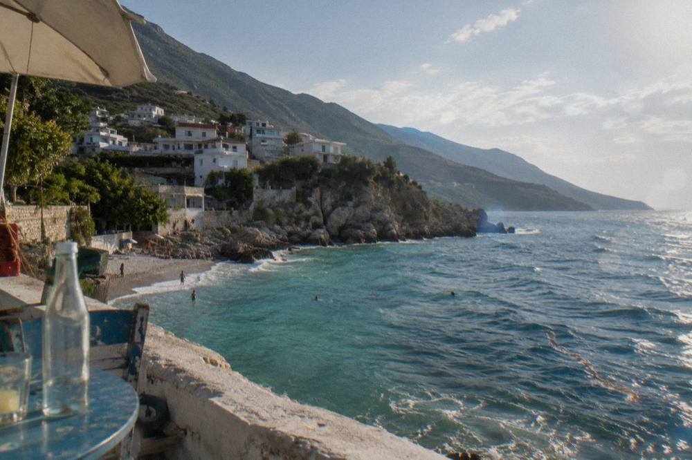 White houses on a hillside above a small pebble beach with clear water