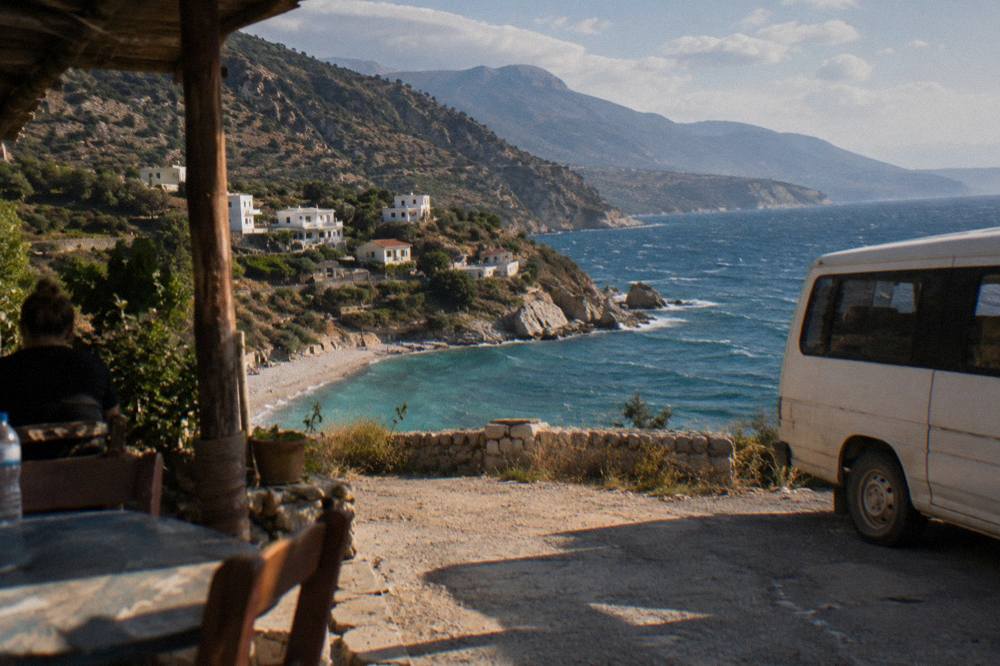 A small white bus parked at a roadside stop above the sea