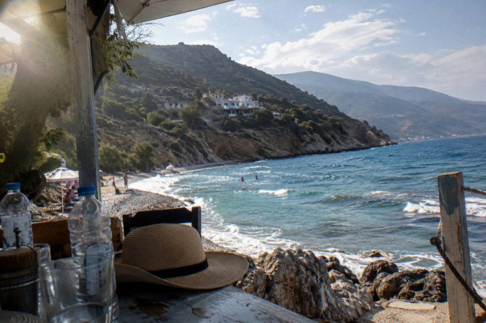 A shaded cafe table with water bottles and a wide-brimmed hat beside the sea