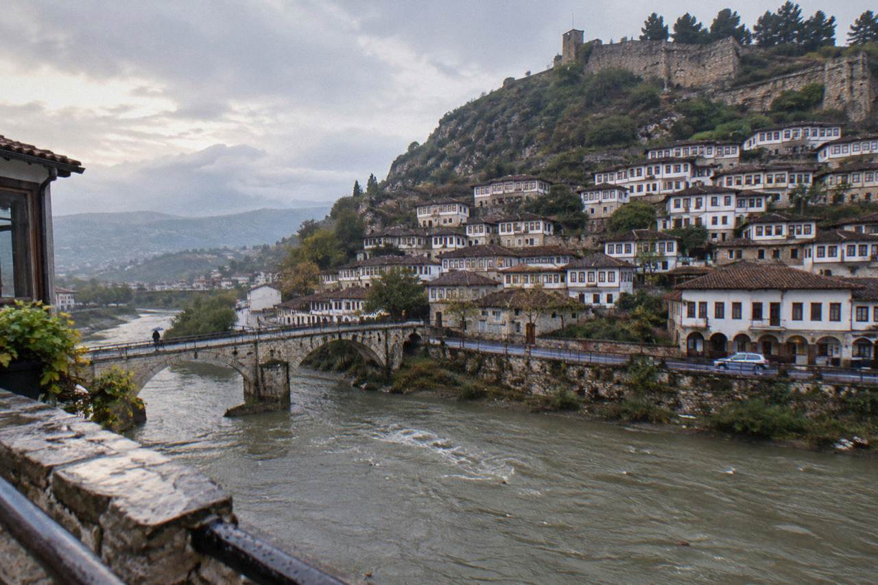 White Ottoman houses stacked on a hillside below a stone castle in Berat
