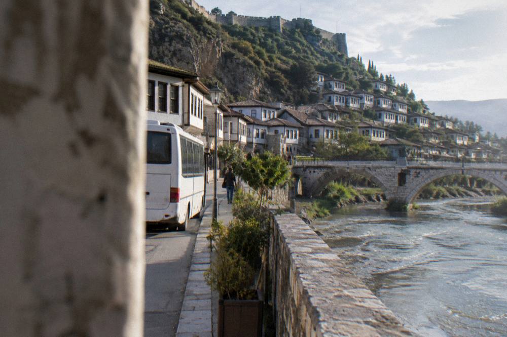 A bus parked on a street beside Ottoman-era houses in a small Albanian town