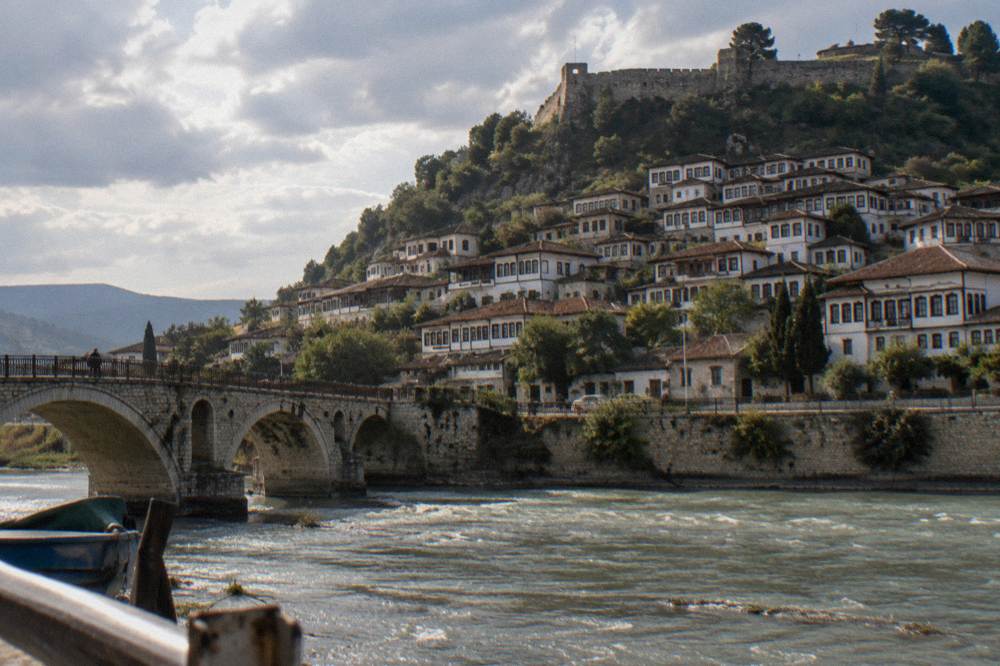 A hillside Ottoman town of whitewashed stone houses with rows of tall windows stacked in tiers up a steep slope above a river