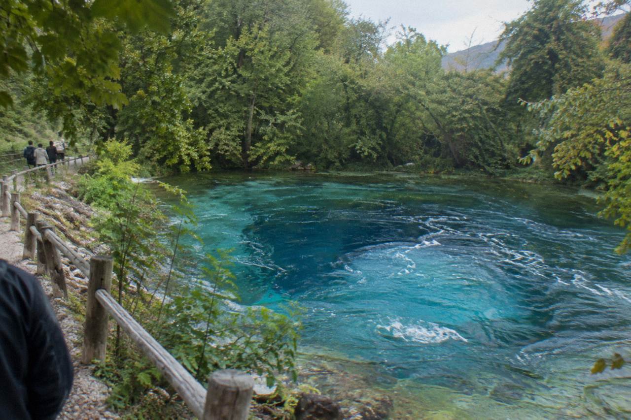 A circular pool of intense blue water surrounded by green trees in southern Albania