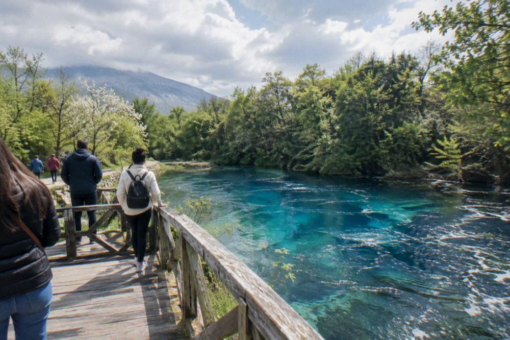 Travellers on a wooden platform above a bright blue spring pool in a green forest