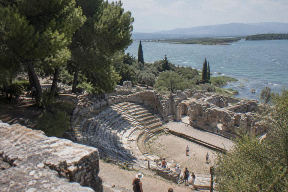 Sunlight over a stone theatre with rows of seats partly shaded by trees