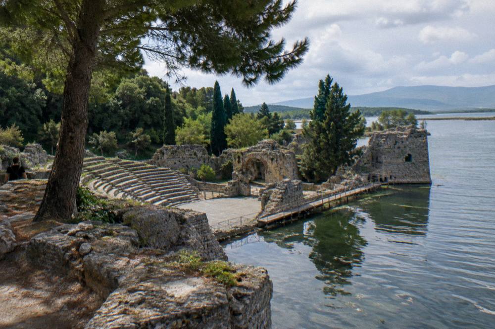 Still water of a lagoon reflecting trees beside ancient stone fortifications