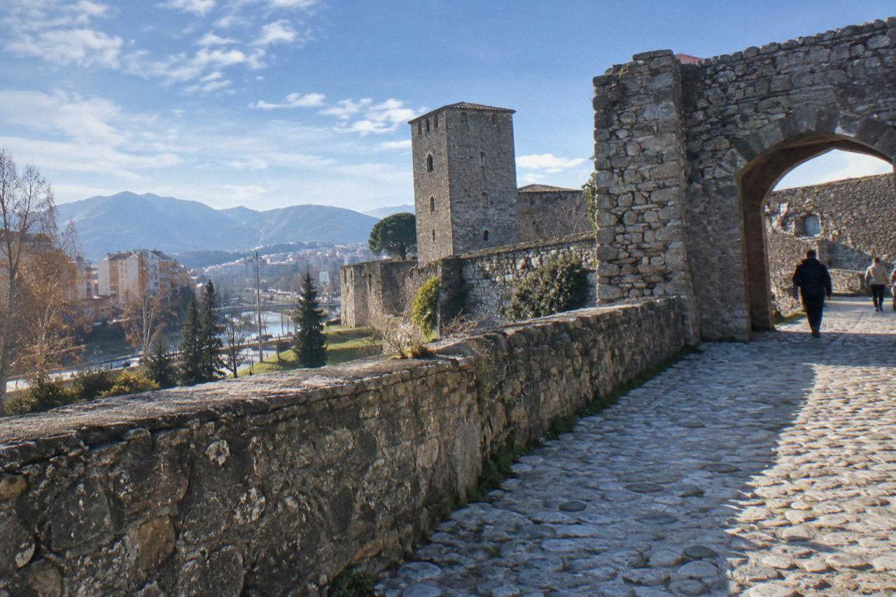 Stone walls and an old gate of Elbasan castle under a blue sky with a cobbled street inside