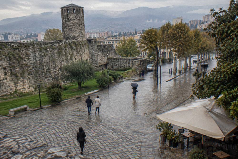 People walking on a cobbled square in Elbasan beside the old town walls