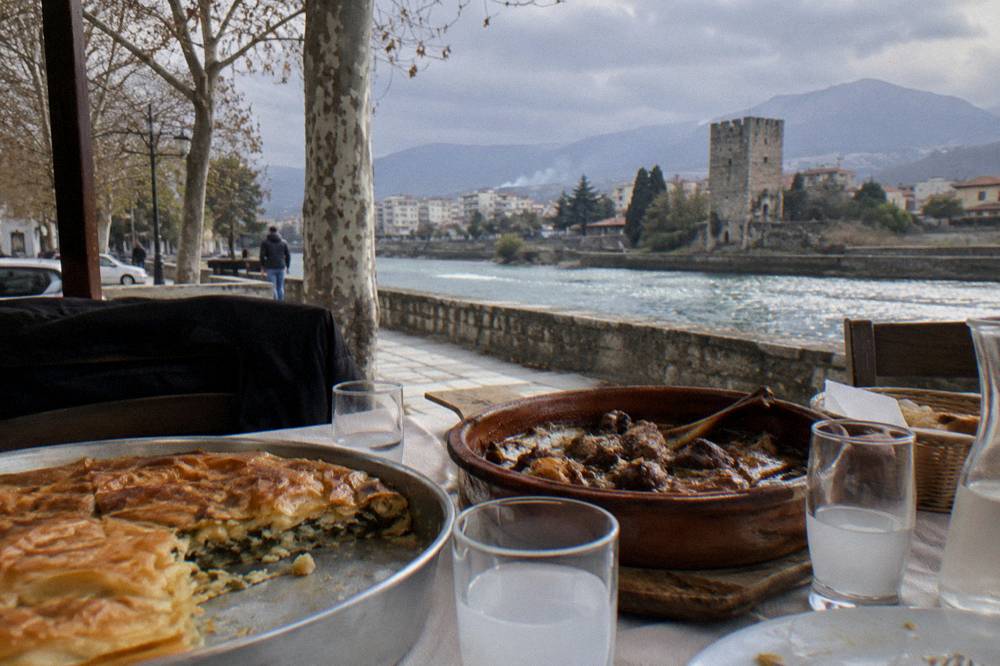 A table with a layered byrek pie, a clay dish of baked lamb and small glasses of raki
