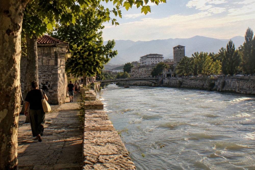 An old town street in warm late afternoon light with stone walls and green trees