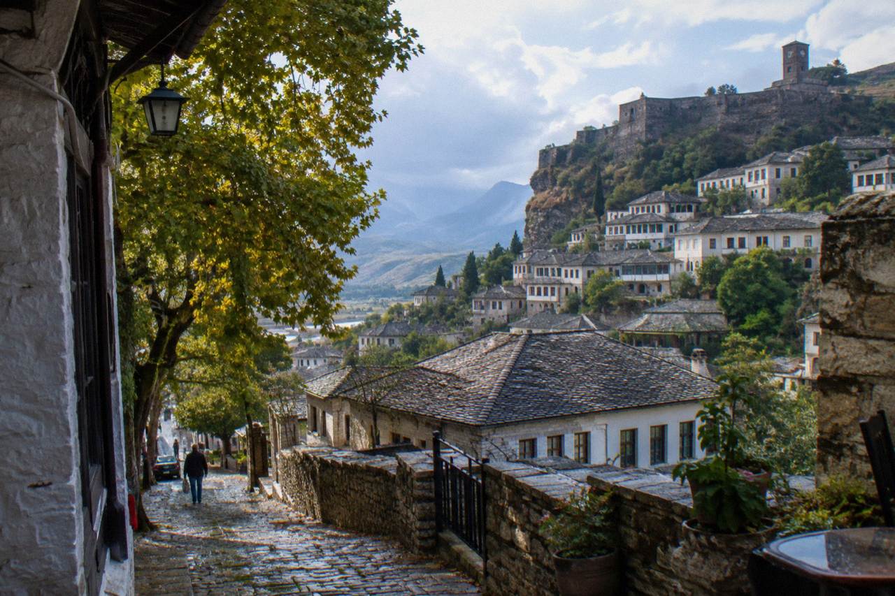 Stone-roofed Ottoman houses stacked on a steep hillside below a castle in Gjirokaster