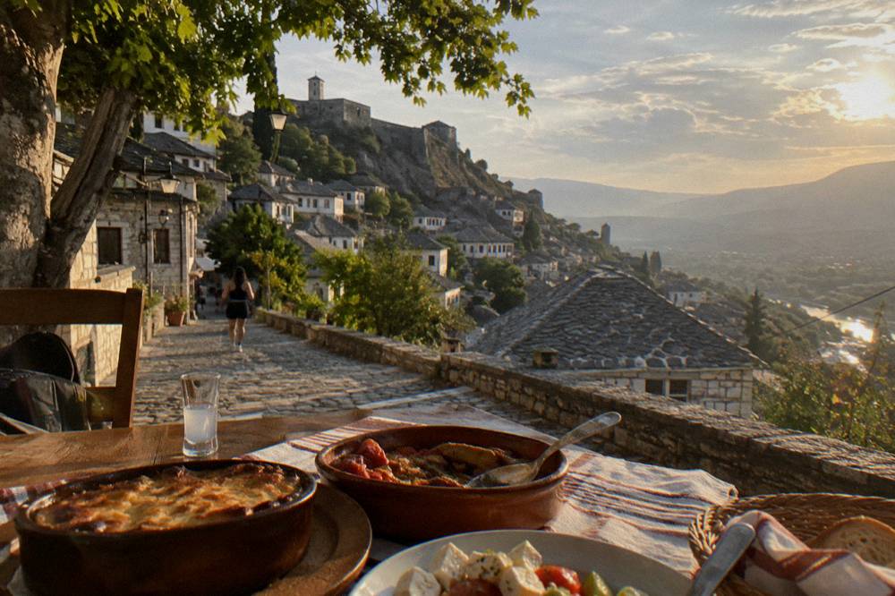 A traditional Albanian restaurant table with baked dishes and a small glass of raki in Gjirokaster