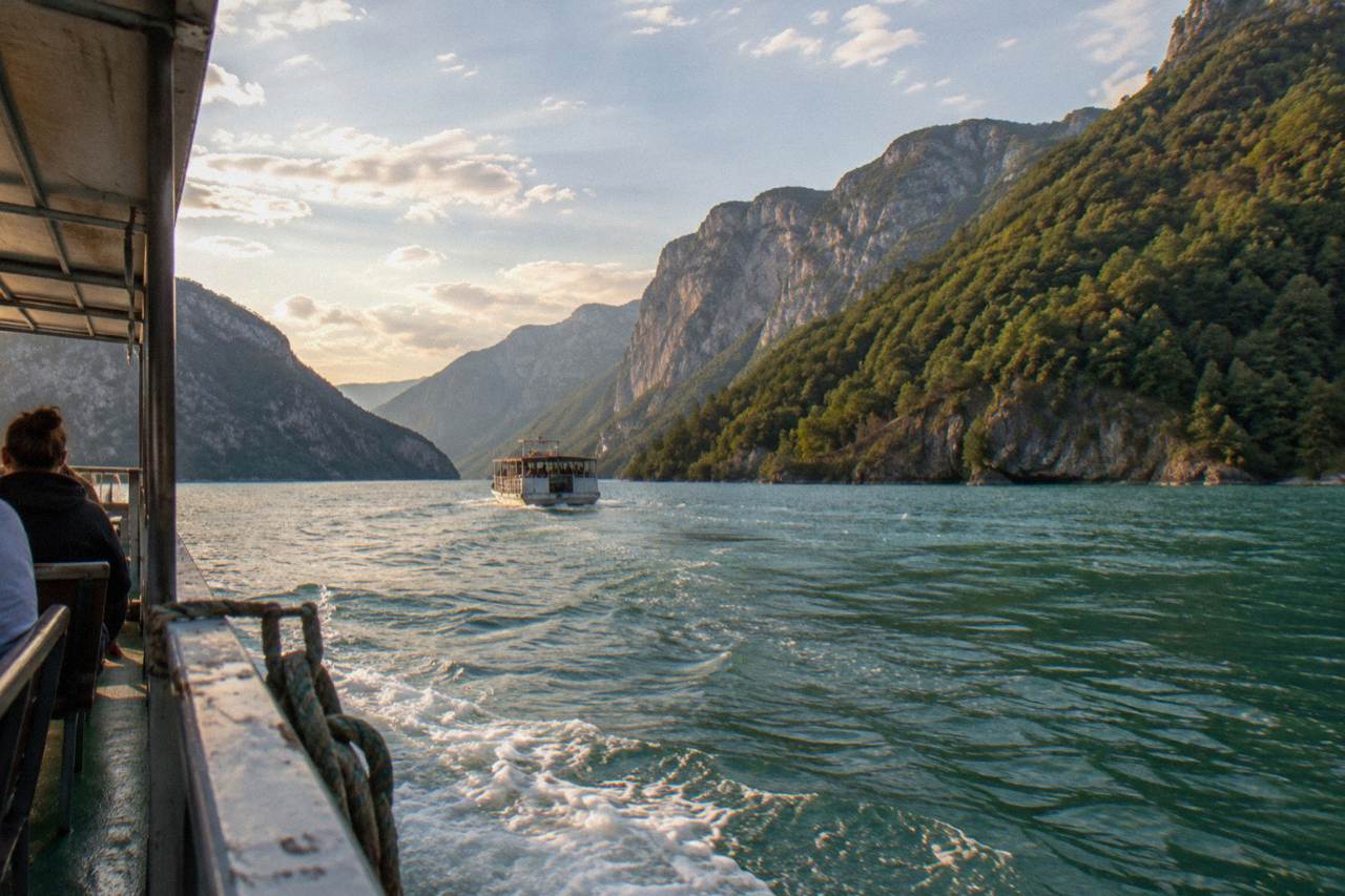 A boat crossing a narrow stretch of turquoise water between steep green hills at Komani Lake