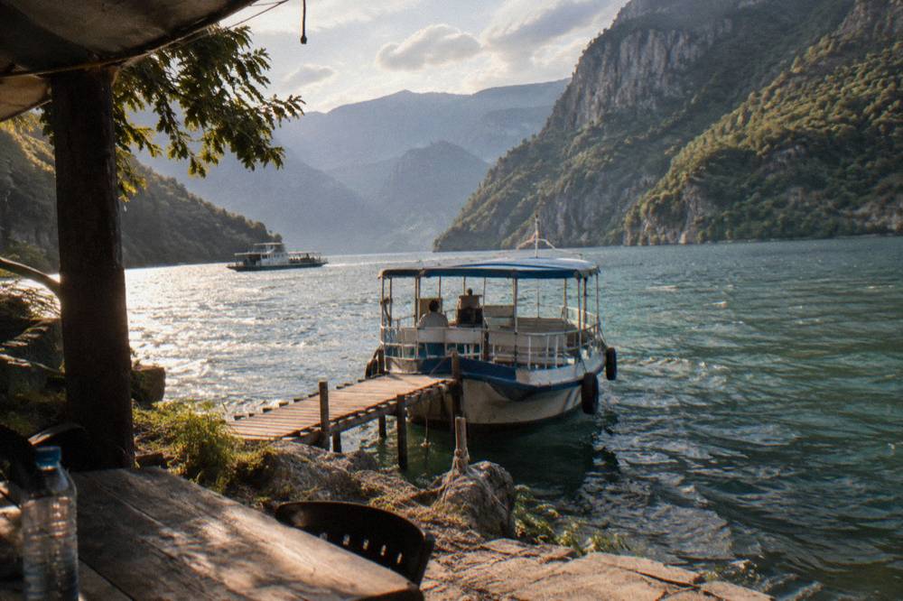 A small passenger boat moored at a wooden jetty on the shore of Komani Lake