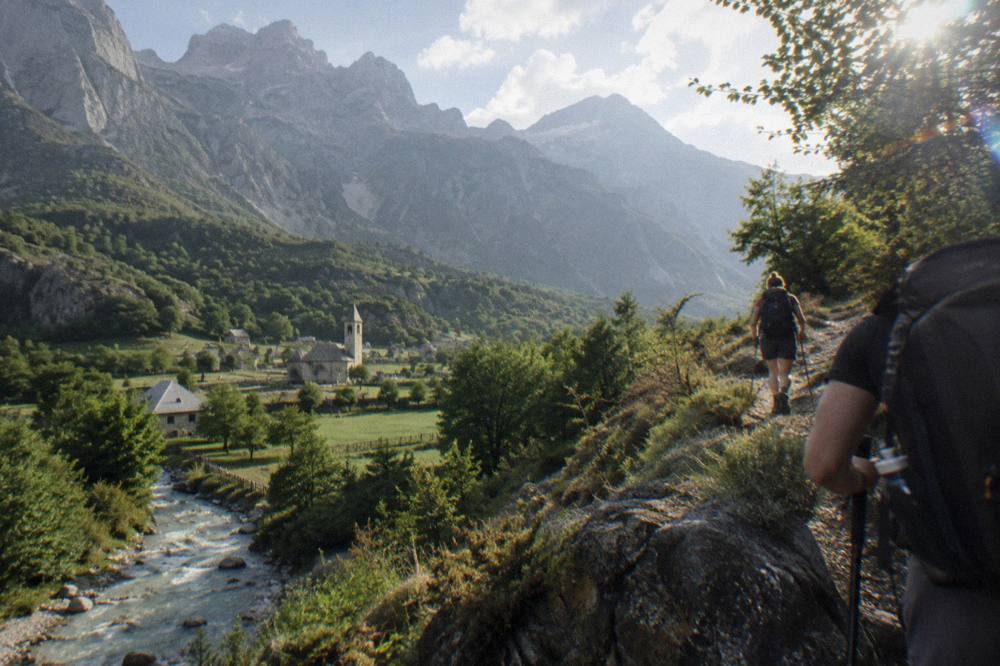 Hikers on a mountain trail above a green valley in the Albanian Alps