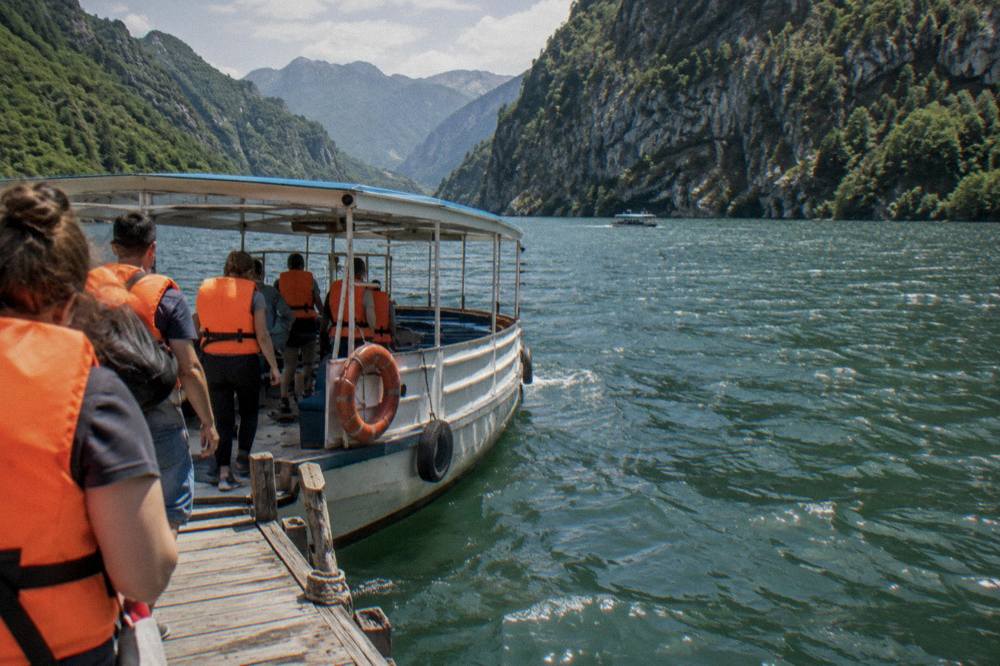 Travellers in life jackets boarding a small tour boat at a wooden pier