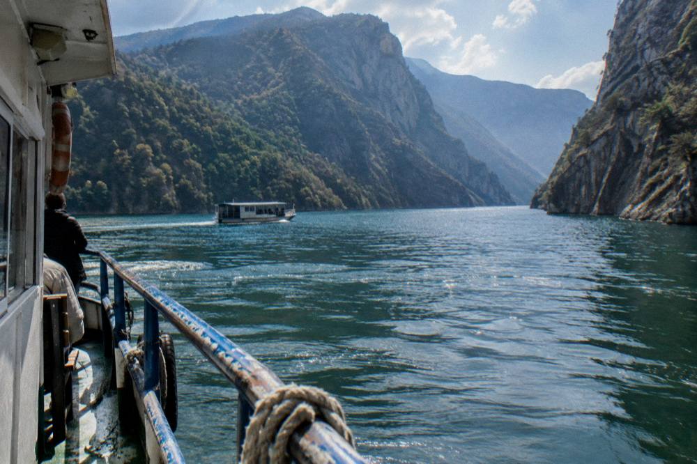 Sunlight on still blue water between high canyon walls at midday on Komani Lake