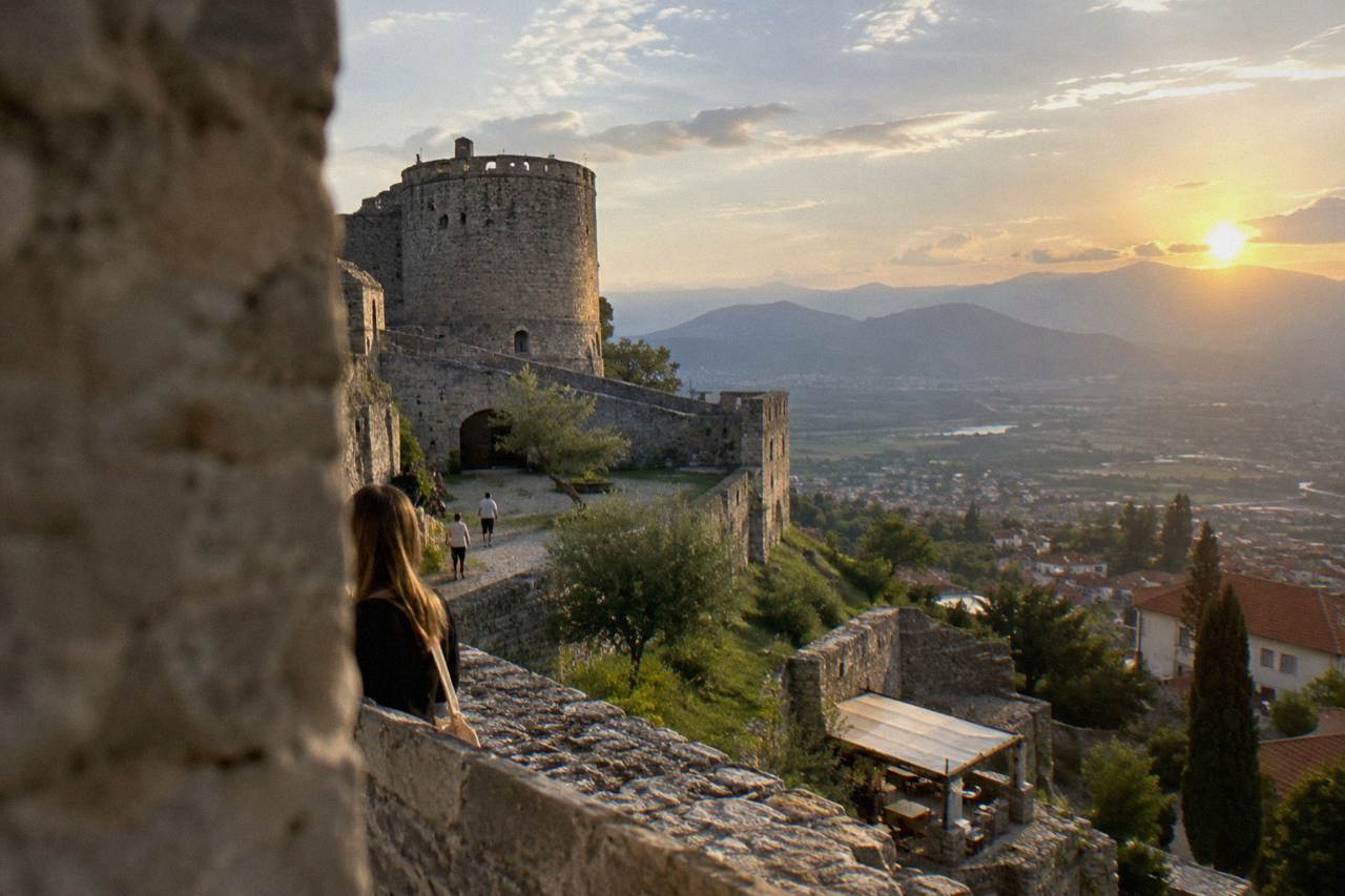 Stone walls and a tower of Kruja Castle on a hillside above a town