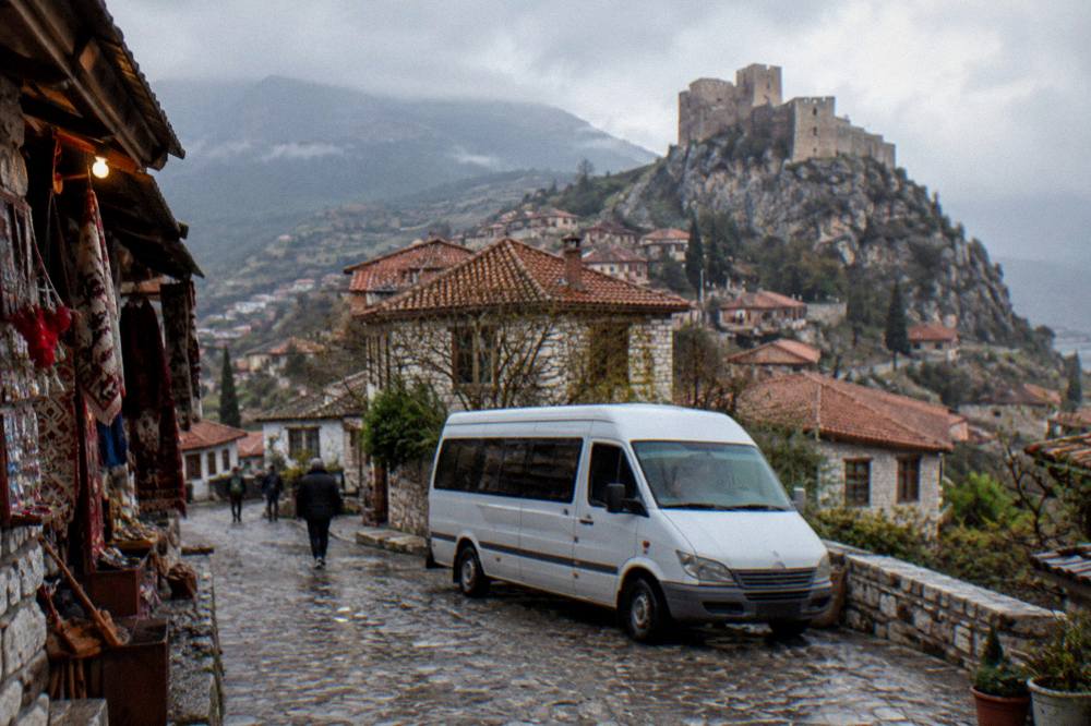 A small minibus parked on a town street with hills behind it