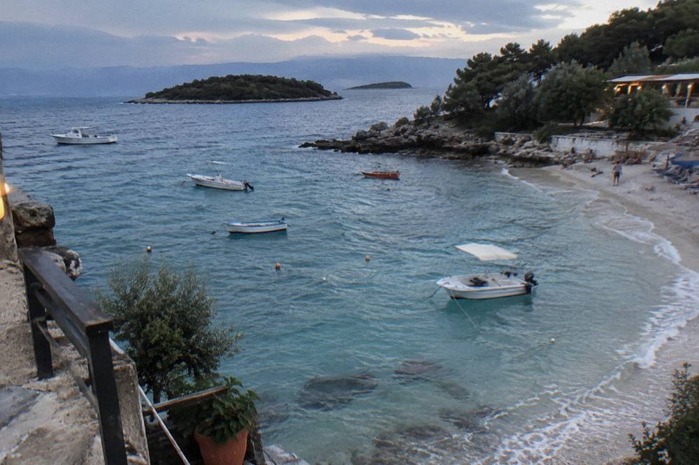 Small boats moored in shallow clear water beside a sandy cove in Ksamil