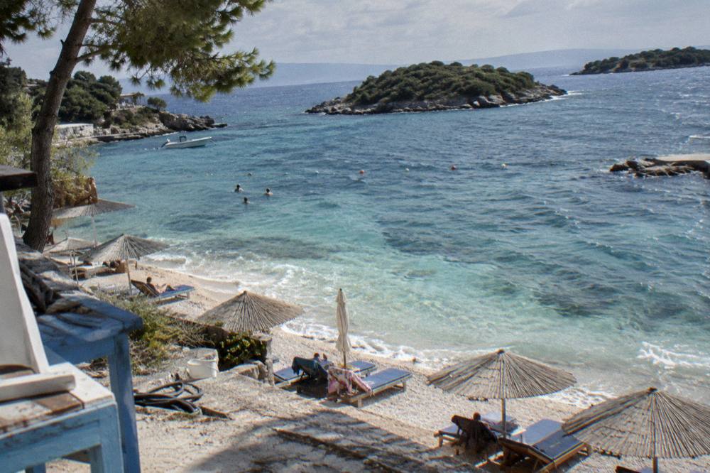 Sun loungers and umbrellas on white sand beside calm turquoise shallows in Ksamil