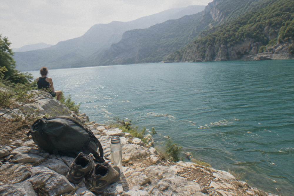 A daypack, walking shoes and a water bottle resting on rocks overlooking a reservoir