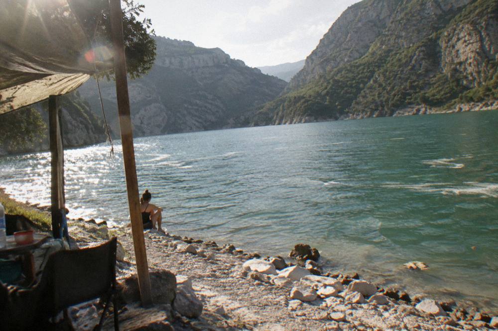 A wide view of a steep-sided canyon holding a still green lake between mountains