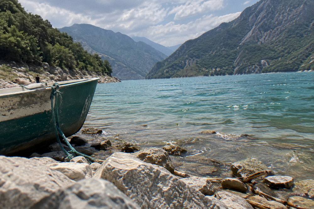 A calm green lake at the foot of grey mountains under scattered clouds