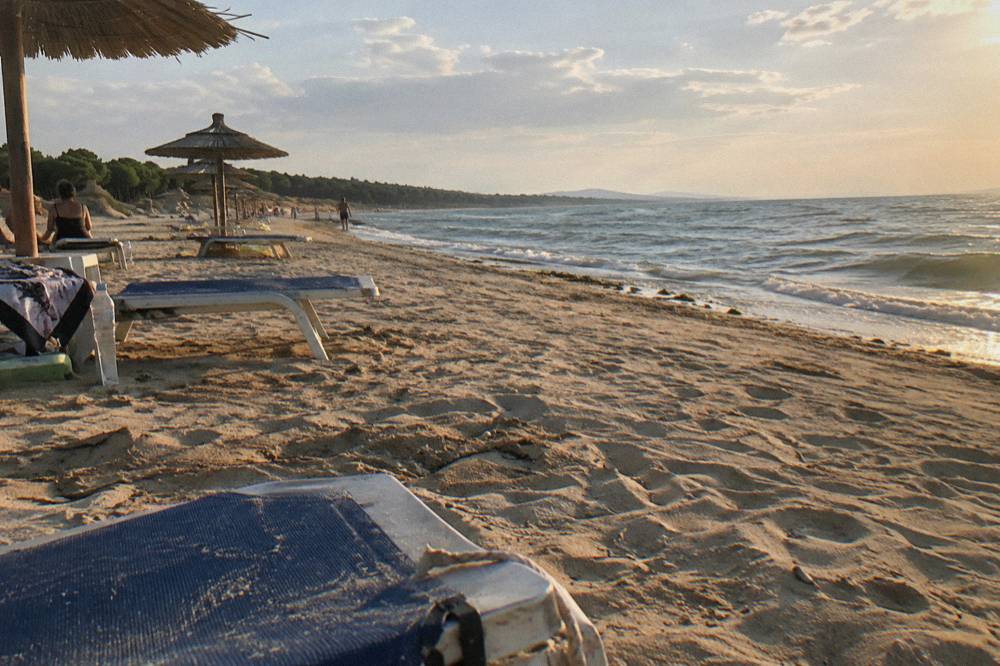 Sunbeds and parasols spaced along a wide sandy beach with calm sea beyond
