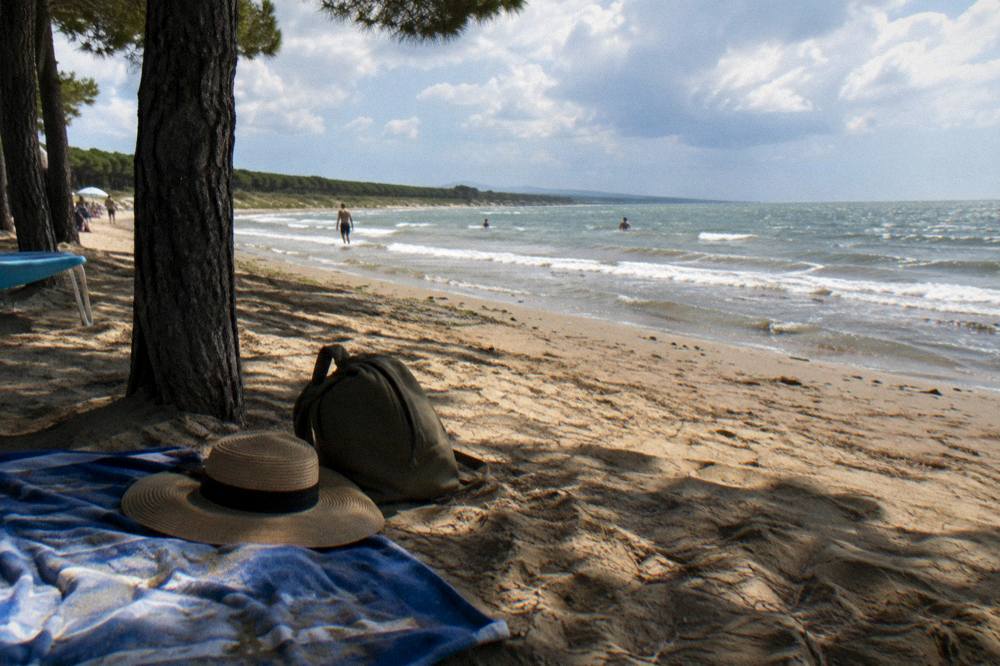 A towel, sunhat and bag resting on sand beside gentle wave lines