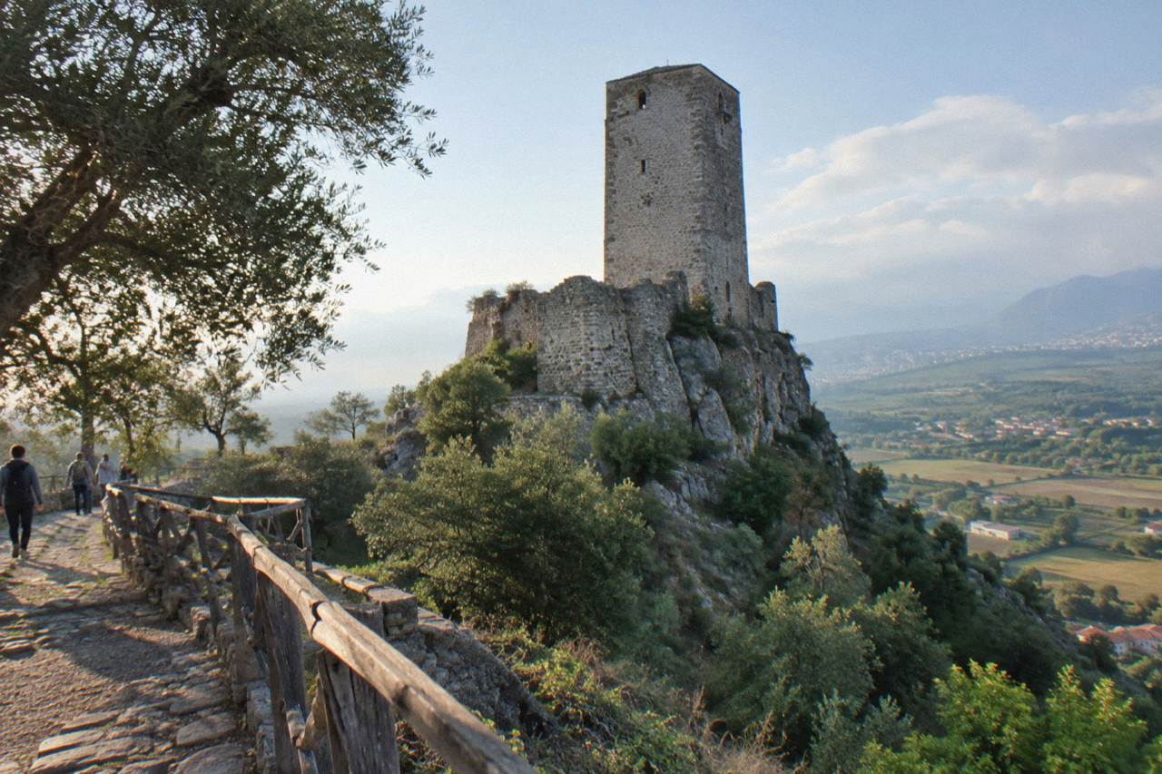 A stone castle tower on a wooded hill above farmland south of Tirana under a clear sky