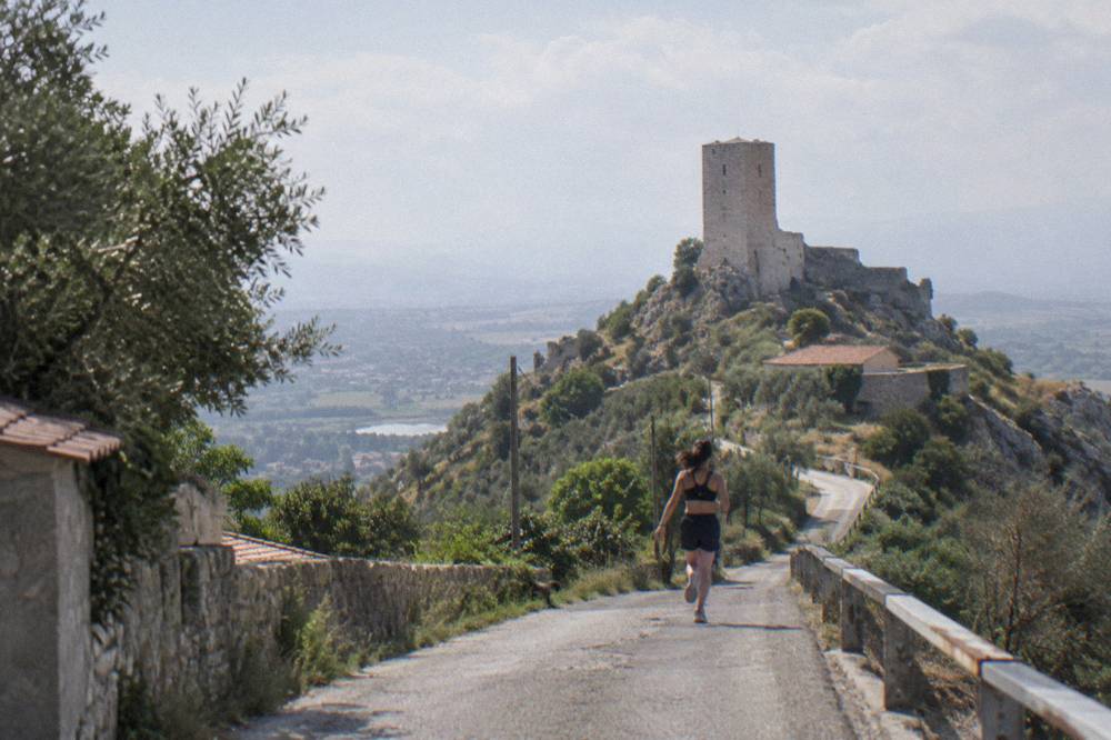 A narrow village road curving up toward a castle on a hill in the Albanian countryside