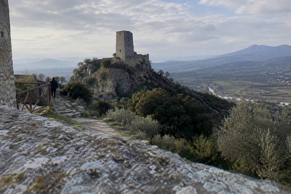 A stone castle tower on a hill with green ridges fading into haze in the distance
