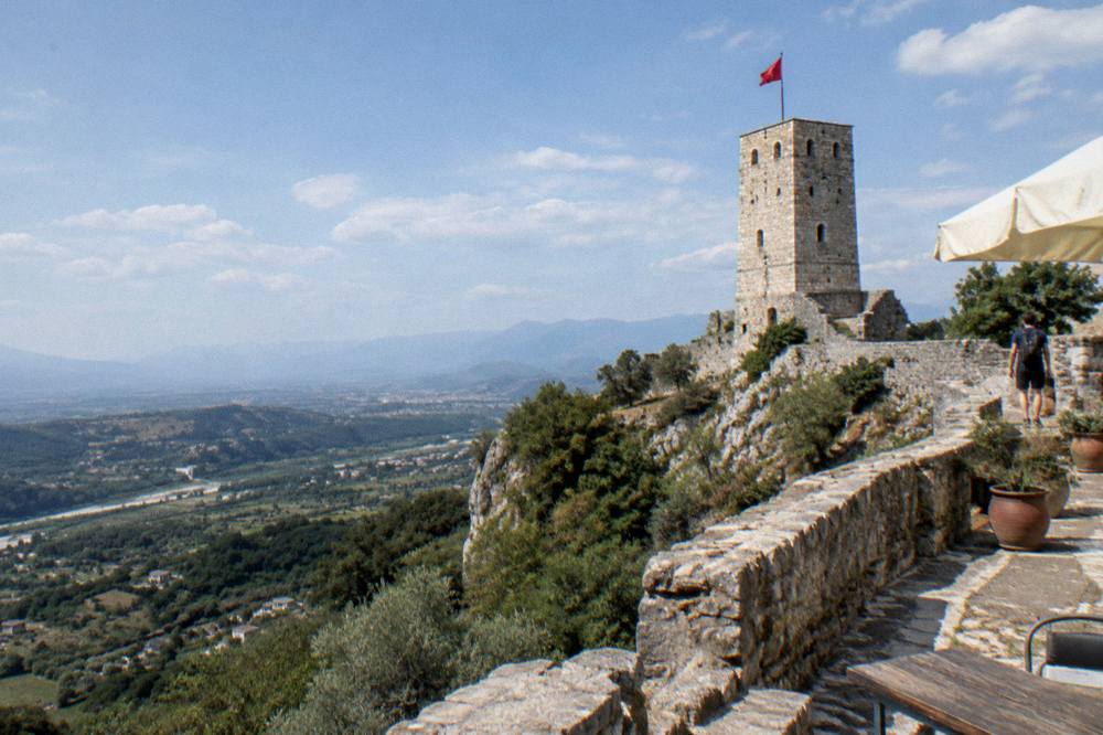 A stone tower with a flag against blue sky, seen from a castle terrace