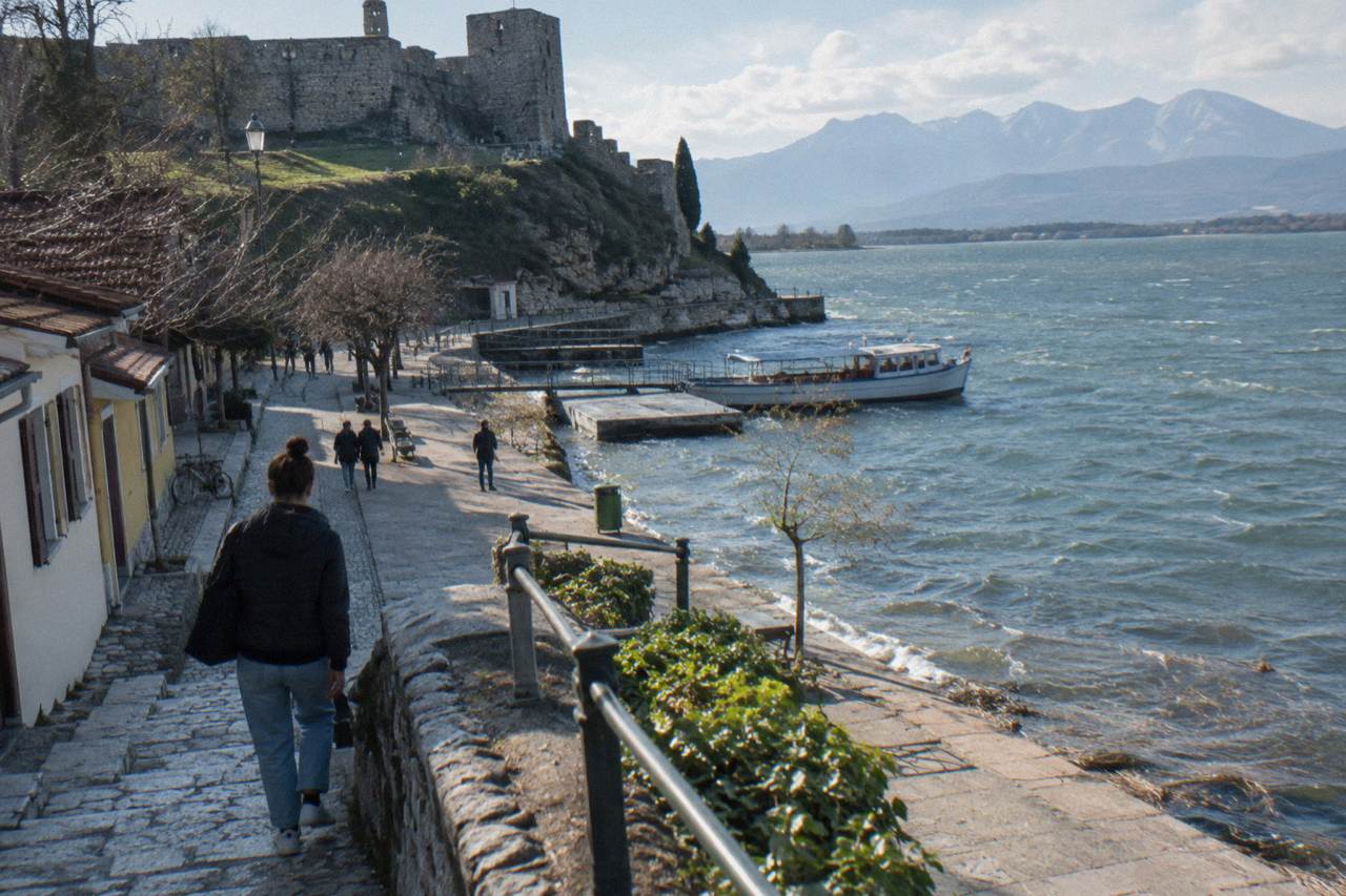 A stone castle wall on a hill above a wide lake and distant mountains