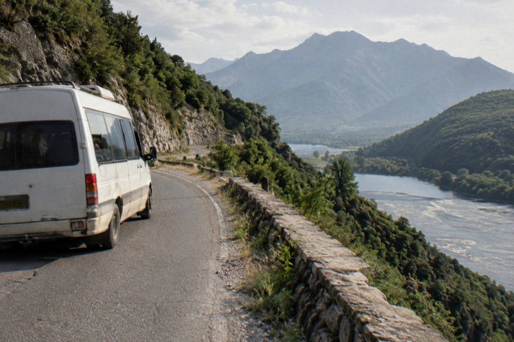 A minibus on a mountain road between steep green slopes