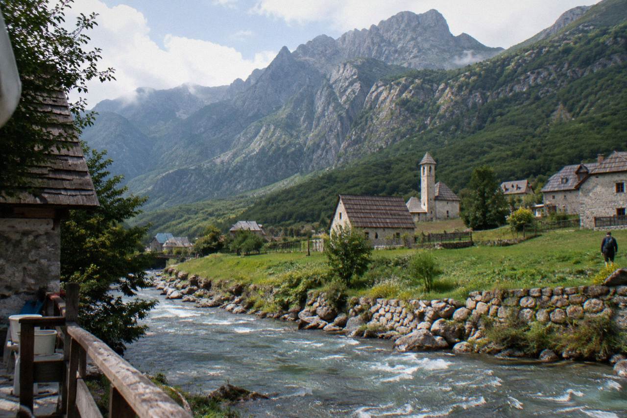 Stone houses with wooden shingle roofs in a green valley below steep mountain slopes